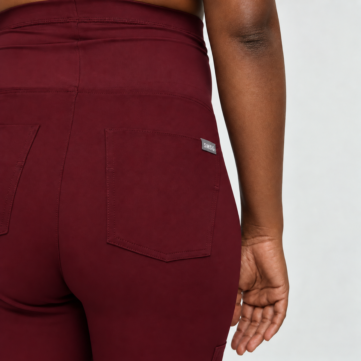 Back view of burgundy SMSG maternity jogger pants showing dual back pockets with woven label SMSG tag detail