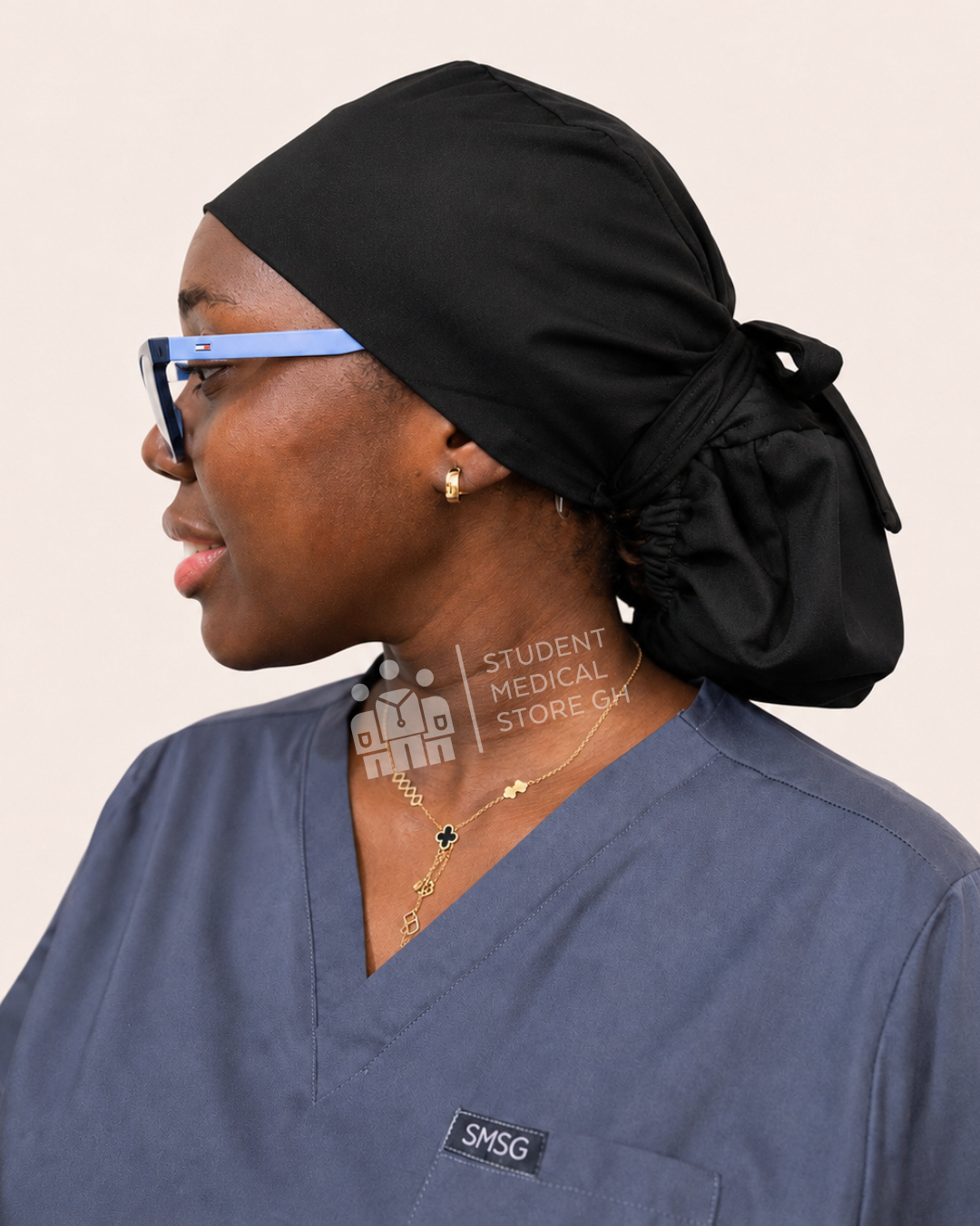 Female nurse wearing grey scrubs  and glasses with a left side view of SMSG black scrub cap.