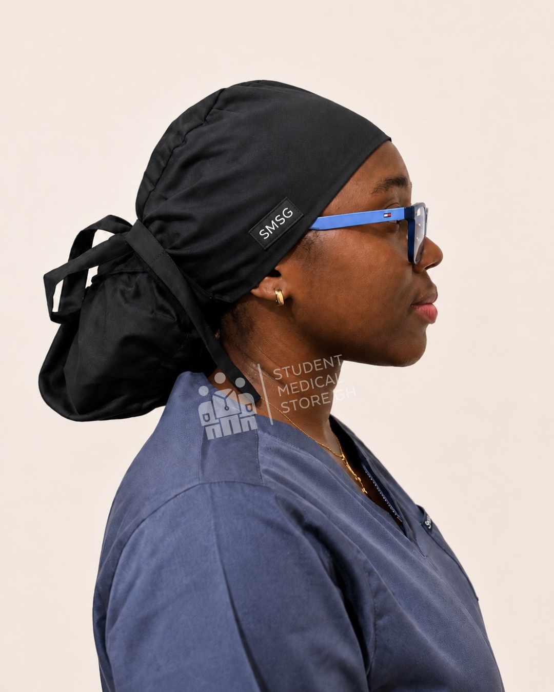 Person wearing grey scrubs with a side view of SMSG black scrub cap on a female doctor wearing glasses.