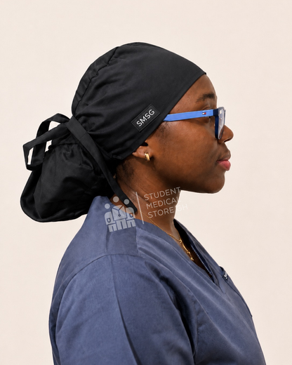 Person wearing grey scrubs with a side view of SMSG black scrub cap on a female doctor wearing glasses.