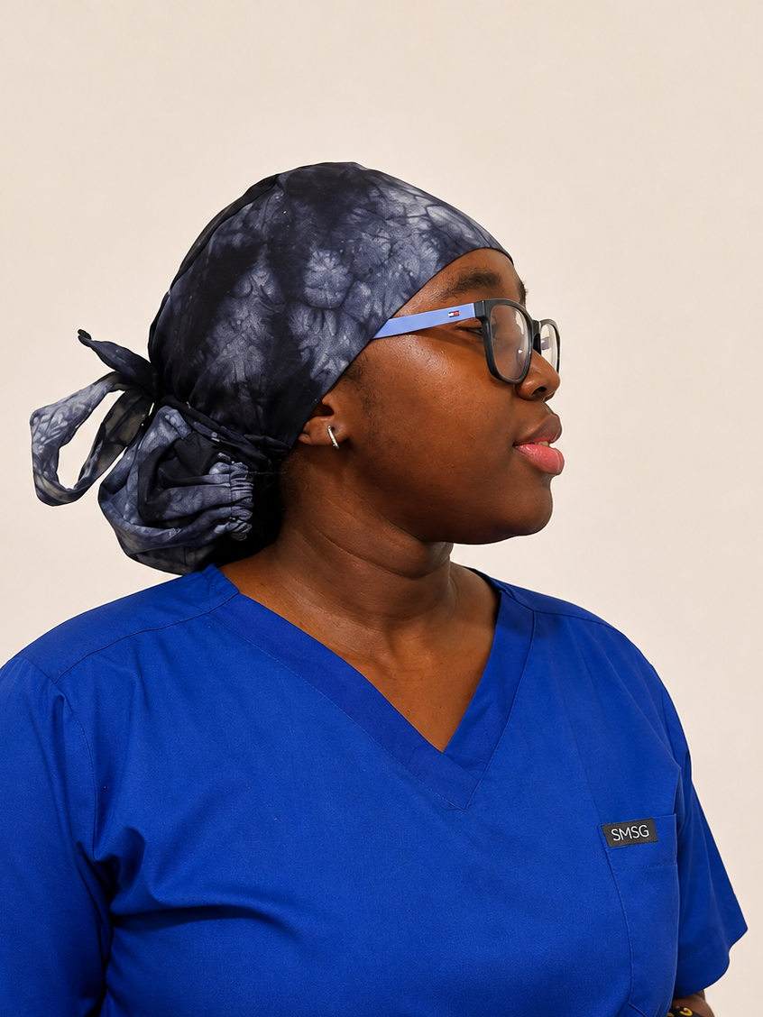 A woman wearing royal blue V-neck medical scrubs and a black patterned scrub cap, shown in profile against a plain beige background.