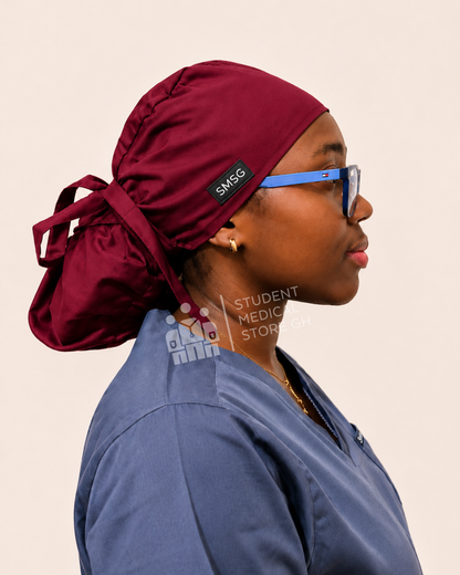 Female nurse wearing grey scrubs  and glasses with a side view of SMSG burgundy blue scrub cap.