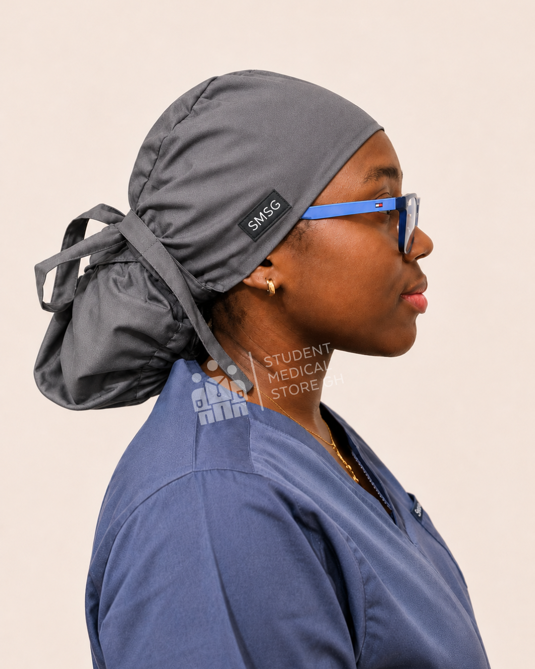 Person wearing grey scrubs with a side view of SMSG grey scrub cap on a female doctor wearing glasses.