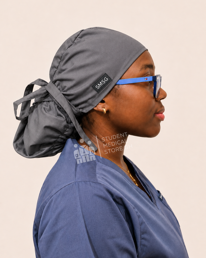 Person wearing grey scrubs with a side view of SMSG grey scrub cap on a female doctor wearing glasses.