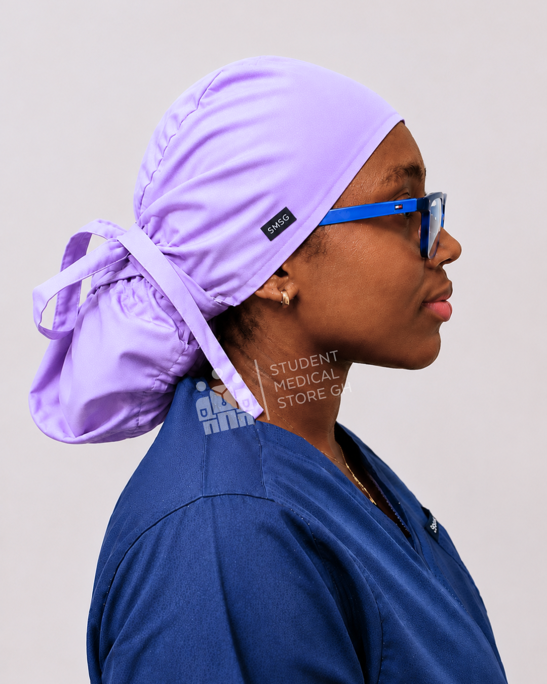 Female doctor wearing grey scrubs  and glasses with a side view of SMSG lilac scrub cap.
