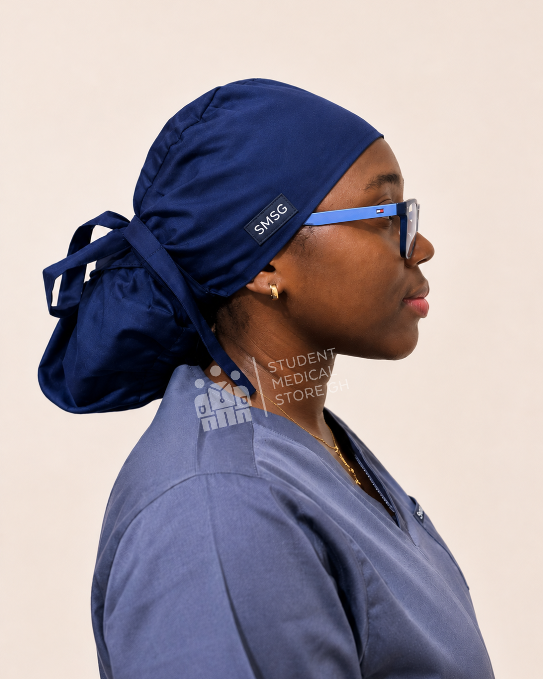 Side view of Person wearing a grey scrub top and SMSG navy blue scrub cap on a beige background