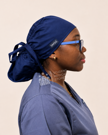 Side view of Person wearing a grey scrub top and SMSG navy blue scrub cap on a beige background