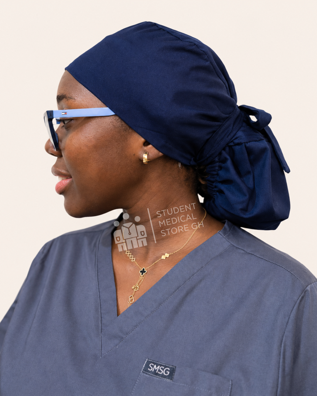 Person wearing navy scrub cap and gray scrubs with 'SMSG' logo on a beige background
