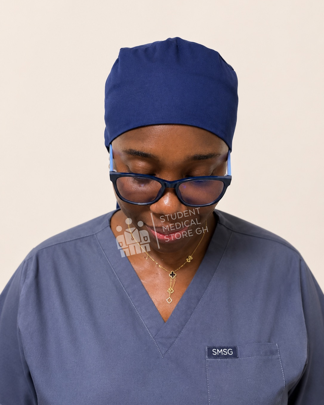 Person wearing grey scrubs with a Front view of SMSG navy scrub cap on a female doctor wearing glasses, looking down.