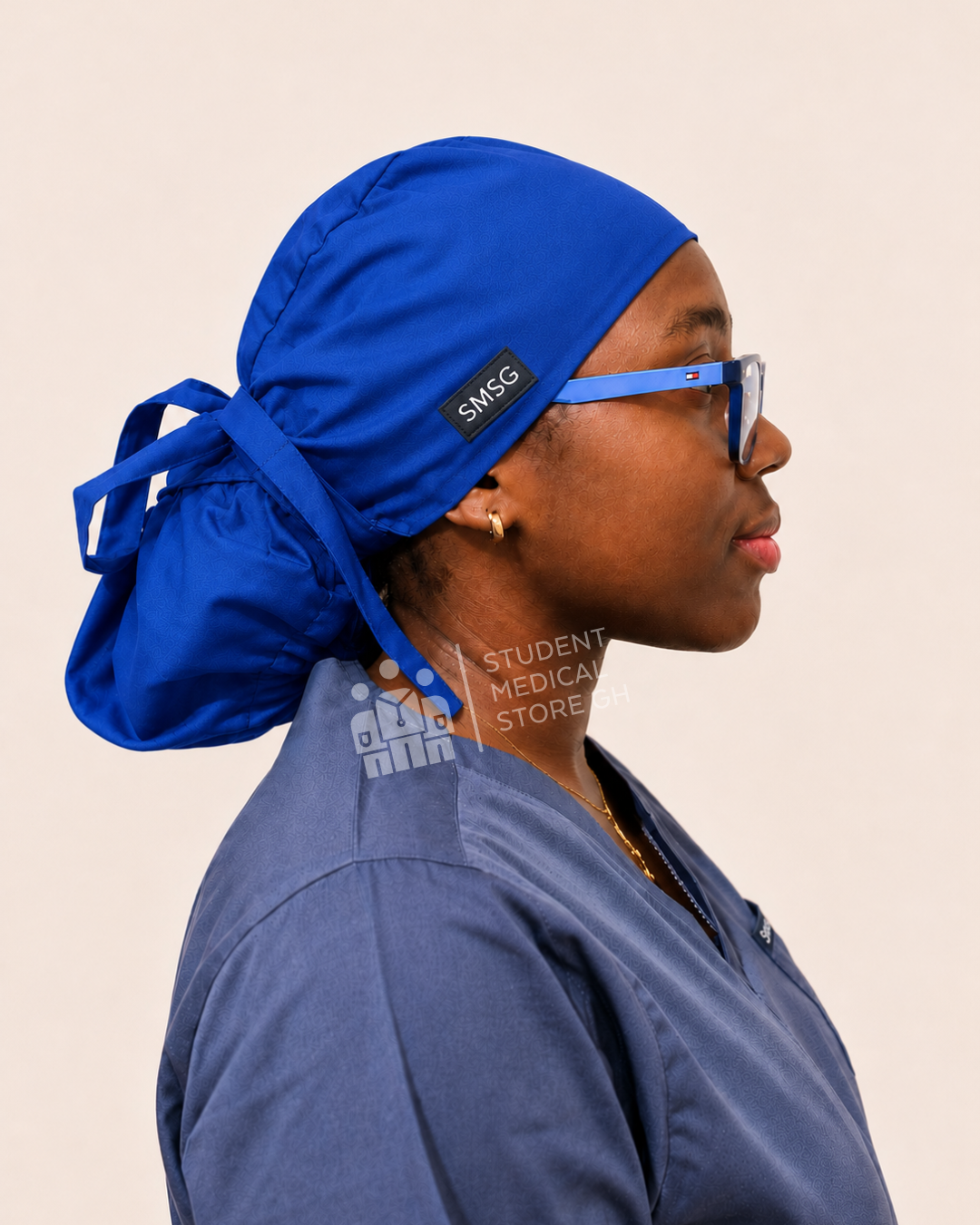 Female nurse wearing grey scrubs  and glasses with a side view of SMSG royal blue scrub cap.