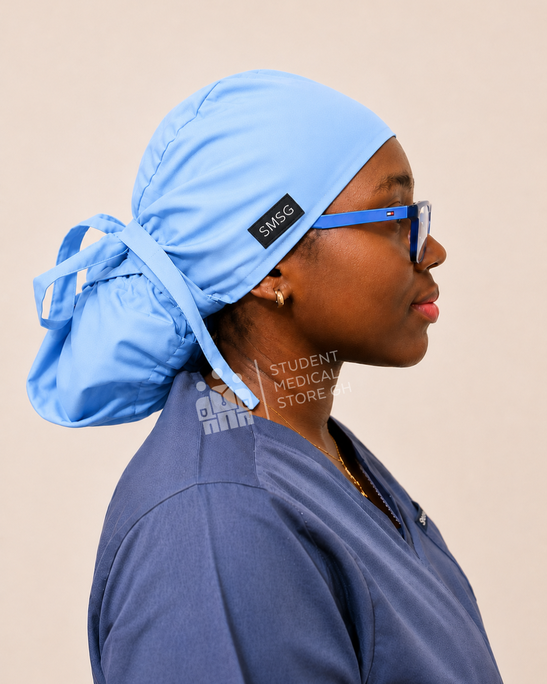 Female nurse wearing grey scrubs and glasses with a side view of SMSG light blue scrub cap.