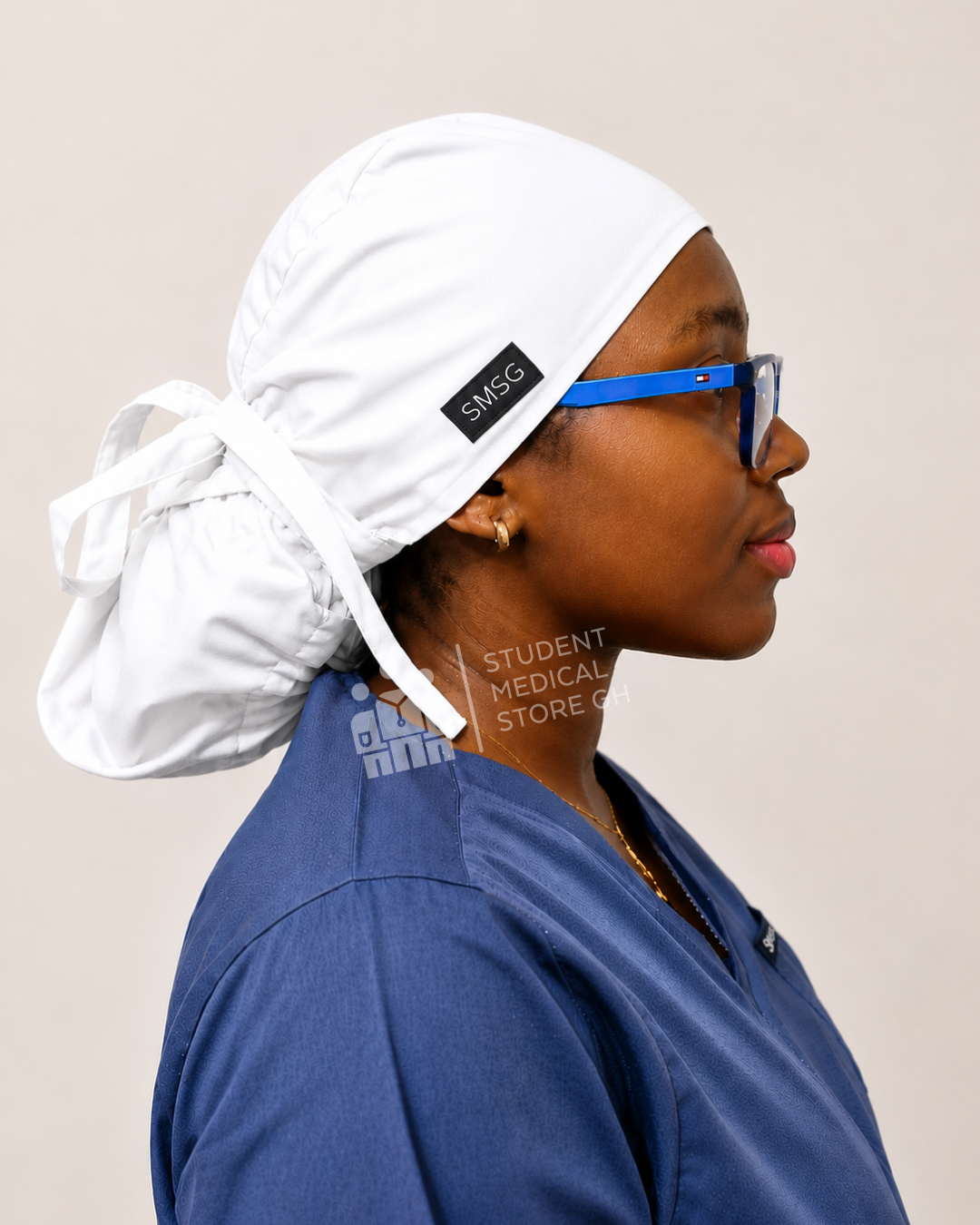 Female nurse wearing grey scrubs  and glasses with a side view of SMSG white ponytail scrub cap.